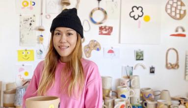 carrie lau in front of her clay art on wall and shelves